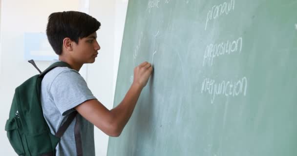 Colegial escribiendo en pizarra verde en el aula — Vídeos de Stock