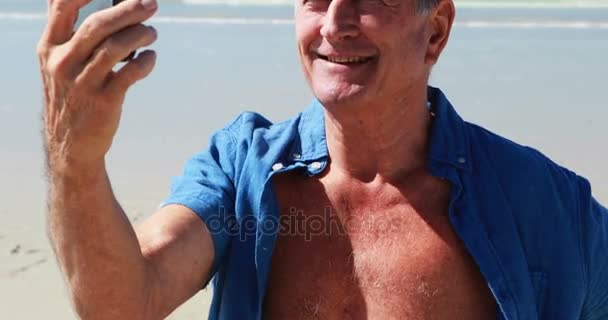 Hombre mayor que tiene videollamada en el teléfono móvil en la playa — Vídeos de Stock