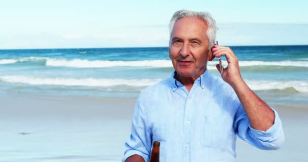 年配の男性がビーチで携帯電話で携帯電話で話しています。 — ストック動画
