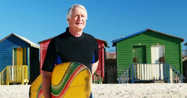 Senior man met surfboard lopend naar de zee — Stockvideo