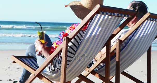 Pareja mayor sentada en una tumbona y tomando un cóctel en la playa — Vídeos de Stock