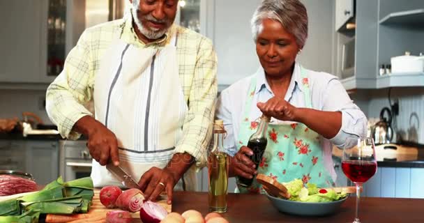 Pria senior memotong sayuran sementara wanita menyiapkan salad di dapur — Stok Video