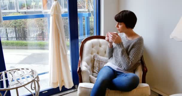 Vrouw op zoek via venster terwijl het hebben van koffie — Stockvideo