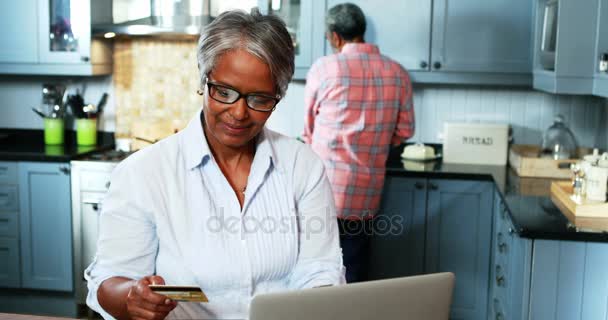 Senior kvinna gör online shopping på laptop i köket hemma — Stockvideo