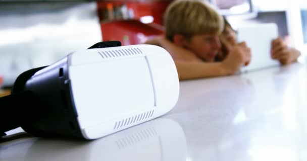 Close-up of virtual reality headset on kitchen worktop while siblings using digital tablet — Stock Video