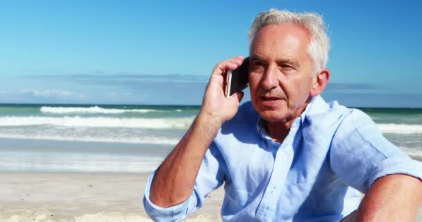 年配の男性がビーチで携帯電話で携帯電話で話しています。 — ストック動画