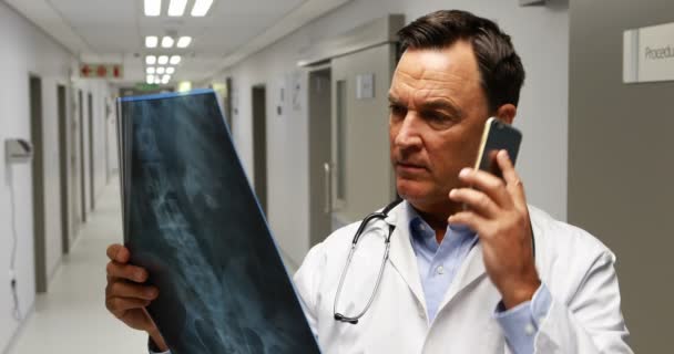 Врач-мужчина разговаривает по мобильному телефону во время разговора по мобильному телефону в коридоре — стоковое видео