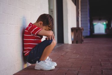 depressed boy crouching by wall at school  clipart
