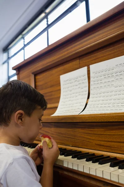 Pojke äta äpple sittande av piano — Stockfoto