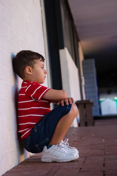 Мальчик, сидящий у стены в школе — стоковое фото