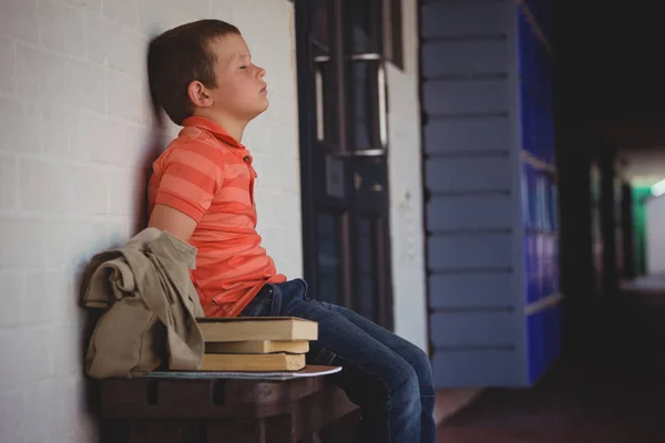 Triste menino sentado em banco por parede — Fotografia de Stock