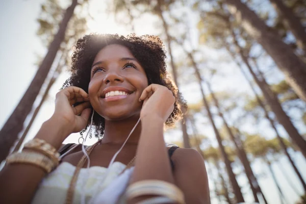 Woman listening music against trees — Stock Photo, Image