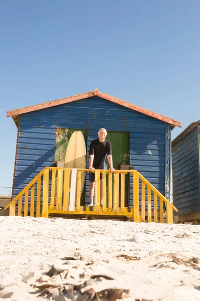 Man standing with surfboard in hut — Stock Photo, Image