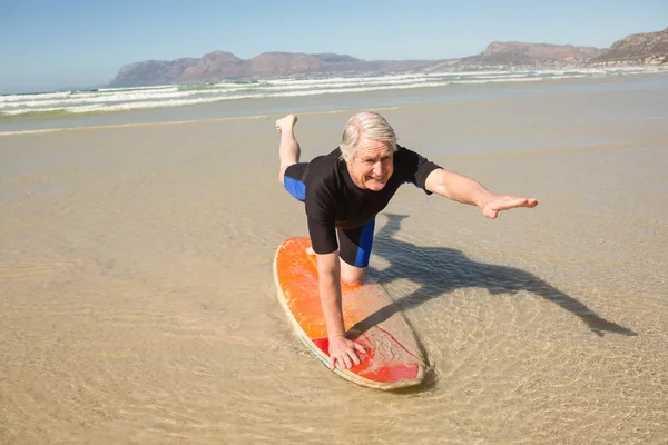 Senior man exercising on surfboard at shore — Stock Photo, Image