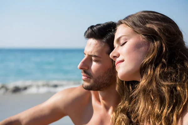 Par med ögonen stängda sittande på stranden — Stockfoto