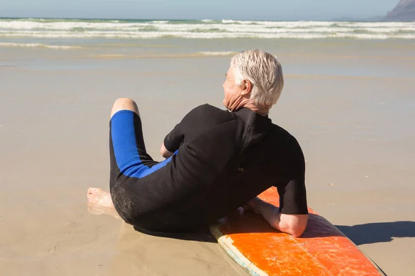 Старший чоловік у гідрокостюмі сидить на дошці для серфінгу — стокове фото