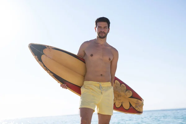 Uomo senza maglietta che tiene tavola da surf in spiaggia — Foto Stock