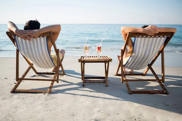 Couple relaxing on lounge chairs at beach — Stock Photo, Image