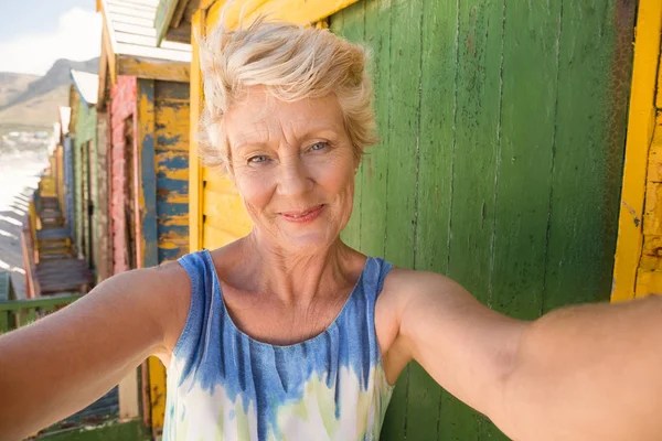 Smiling senior woman against beach hut — Stock Photo, Image
