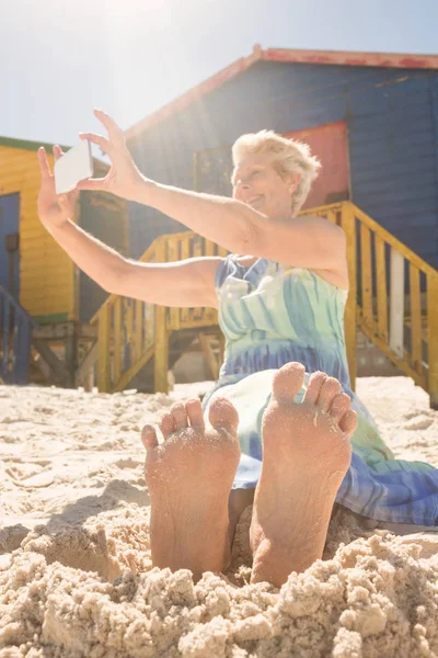 Kobieta za pomocą inteligentnego telefonu siedząc na piasku — Zdjęcie stockowe