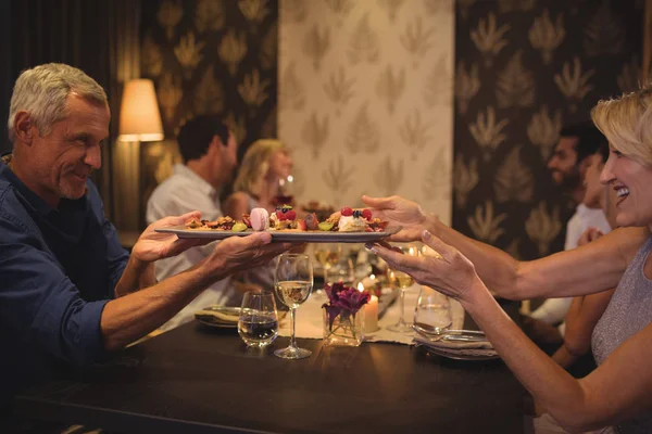 Hombre pasando un plato de comida a la mujer en la mesa —  Fotos de Stock