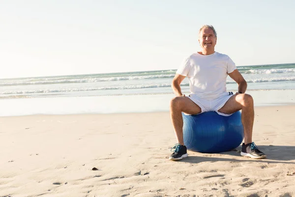 Starší muž, sedící na míč proti moři — Stock fotografie
