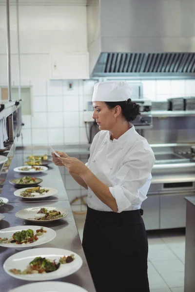 Chef feminino olhando para uma lista de pedidos na cozinha — Fotografia de Stock