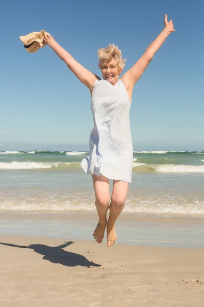 Senior vrouw springen op zand tegen clear sky — Stockfoto