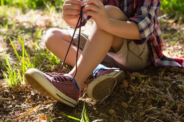 Мальчик завязывает шнурки в лесу — стоковое фото