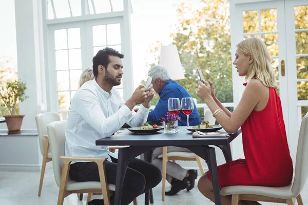 Casal usando telefone durante a refeição — Fotografia de Stock