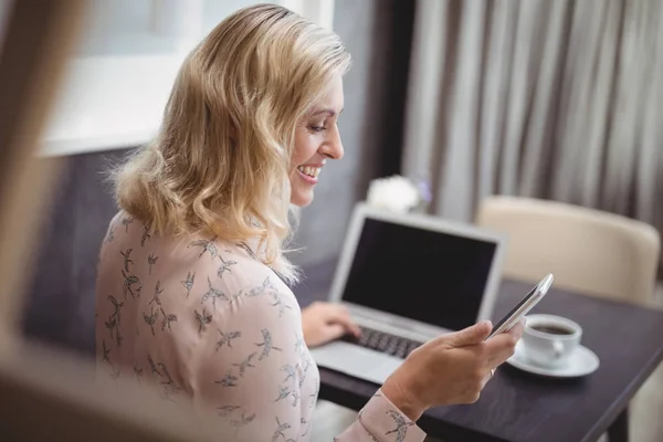 Жінка використовує телефон під час роботи на ноутбуці — стокове фото