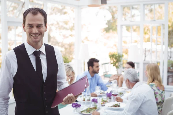 Kelner, trzymając menu podczas przyjaciele jadalnia — Zdjęcie stockowe
