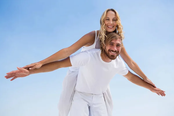 Hombre piggybacking novia contra el cielo — Foto de Stock