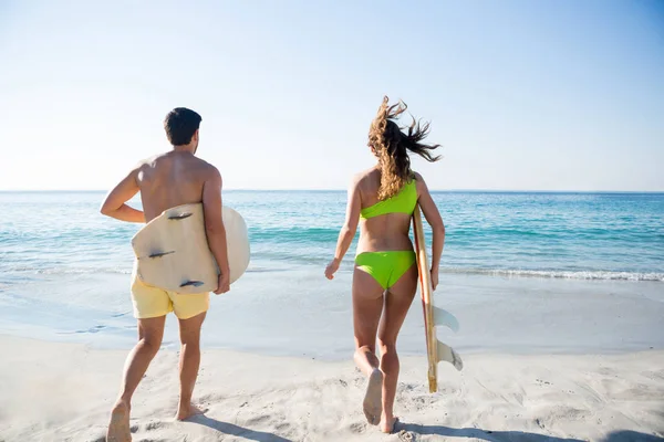 Para uruchomiona trzymając deski surfingowe na plaży — Zdjęcie stockowe