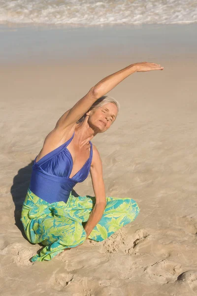 Mulher se exercitando enquanto sentado na areia — Fotografia de Stock