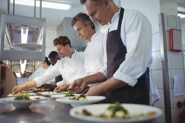 Team of chefs garnishing meal on counter — Stock Photo, Image