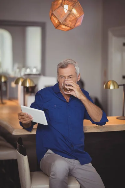 Homme mûr utilisant la tablette tout en ayant de la bière — Photo