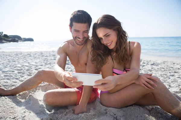 Paret tar selfie medan du sitter på stranden — Stockfoto