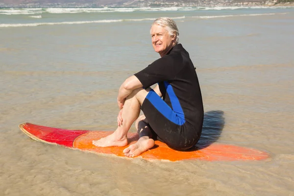 Uśmiechający się starszy człowiek siedzi na deskę surfingową — Zdjęcie stockowe