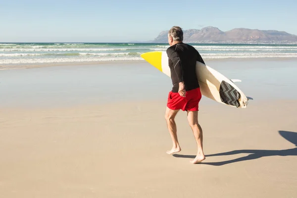 Homem carregando prancha de surf enquanto corre na areia — Fotografia de Stock