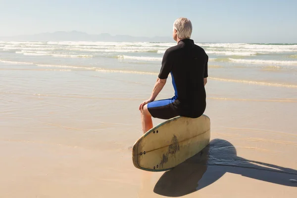 Senior man sitting on surfboard — Stock Photo, Image