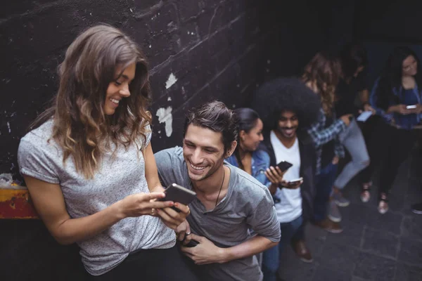 Amis utilisant des téléphones tout en se tenant près du mur — Photo