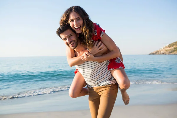Hombre piggybacking alegre novia en playa — Foto de Stock