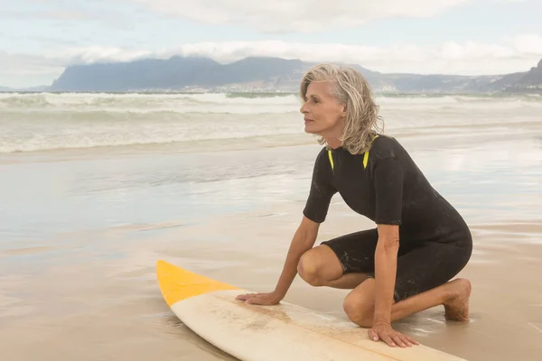 Seniorin kniet mit Surfbrett am Ufer — Stockfoto