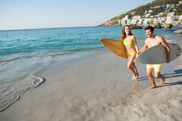 Coppia che corre insieme tenendo in mano tavole da surf — Foto Stock