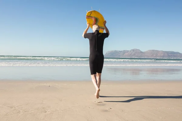 Senior trägt Surfbrett am Strand — Stockfoto