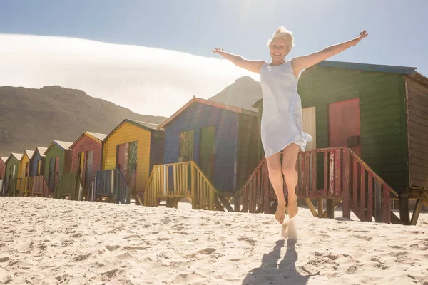 Vrouw springen op zand tegen hutten — Stockfoto