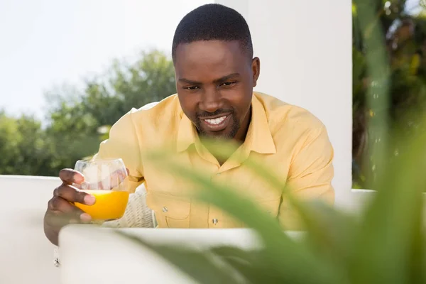 Man holding juice glass looking at laptop — Stock Photo, Image