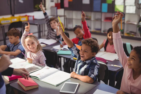 Schoolkids höjer händerna i klassrummet — Stockfoto