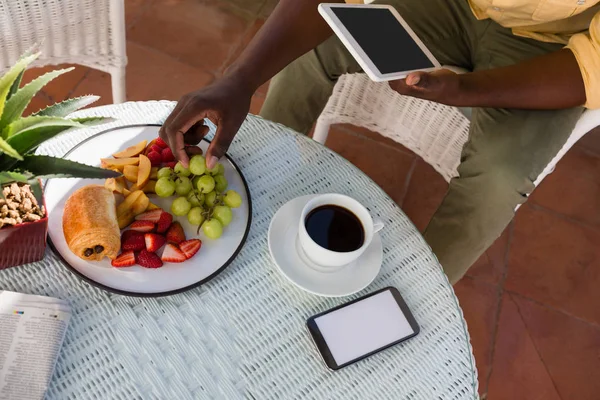 Hombre sosteniendo la tableta mientras tiene uvas — Foto de Stock